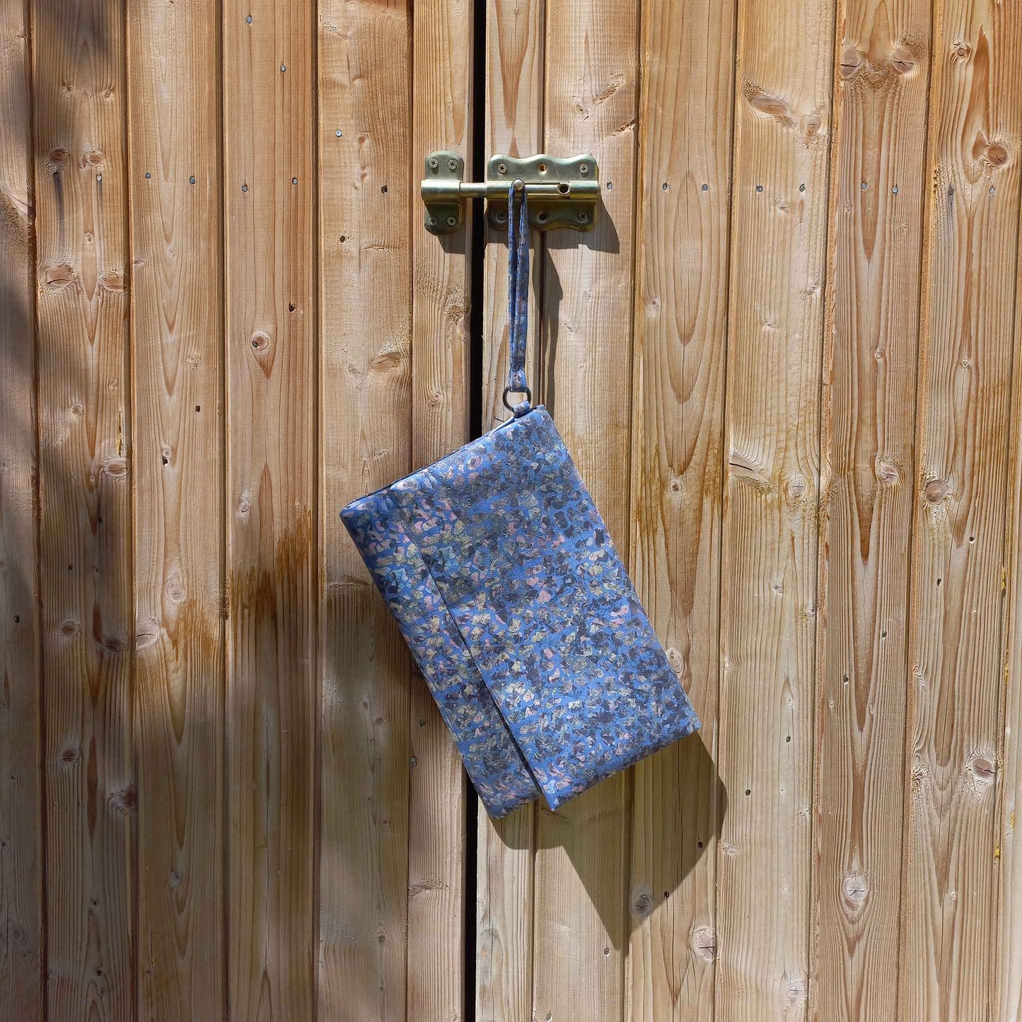 Printed vegan suede clutch bag, hanging from a shed door