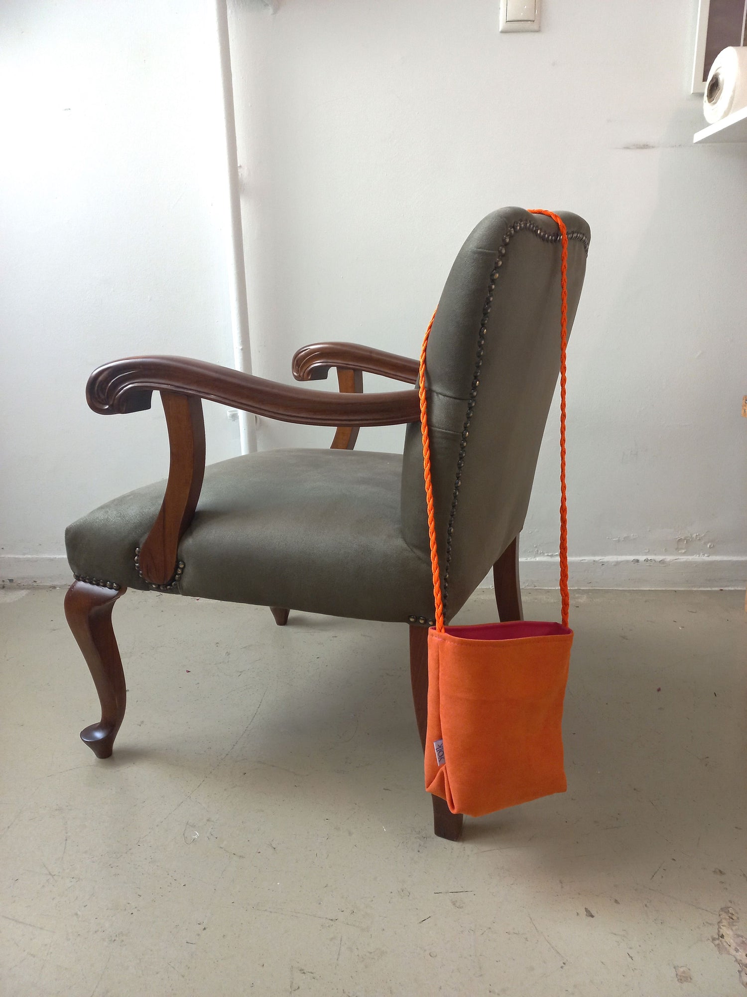Orange bag hanging from a chair against a white wall