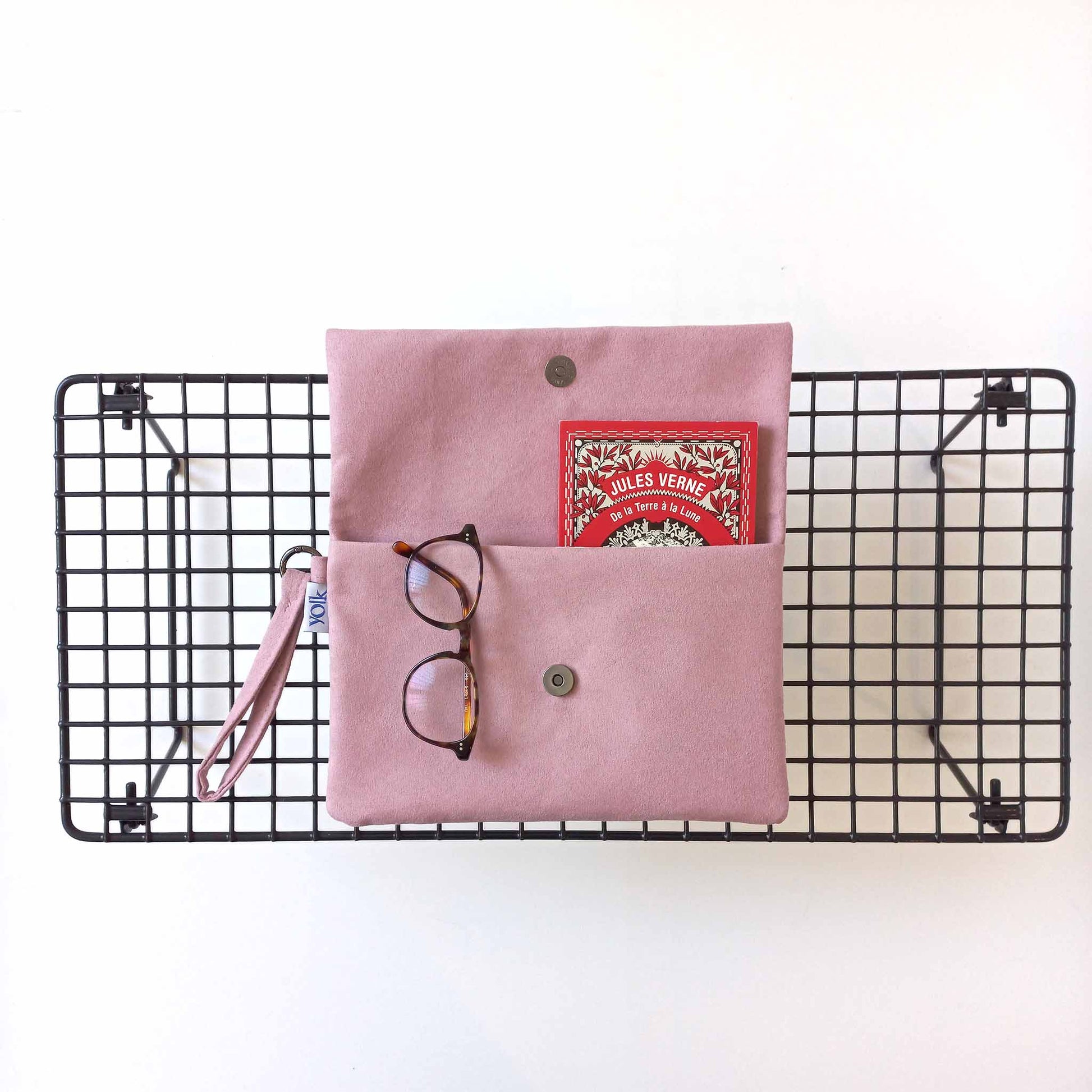 A soft suede pink clutch with a book and glasses