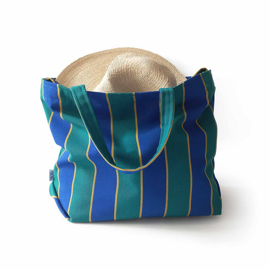 A blue and green beach bag with a straw hat inside it