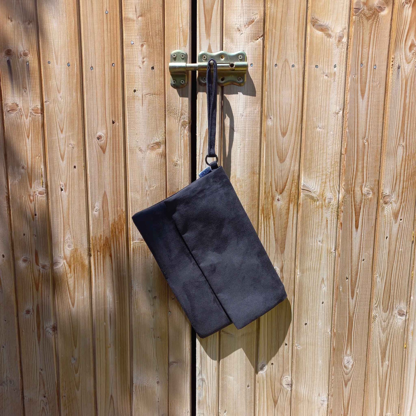 Black suede clutch bag hanging from a shed door