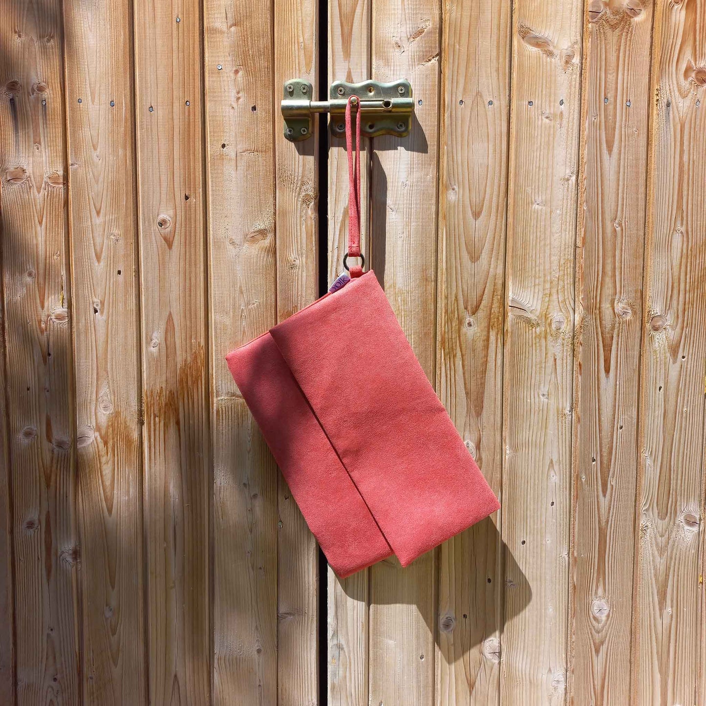 Red vegan suede clutch bag hanging from a shed door