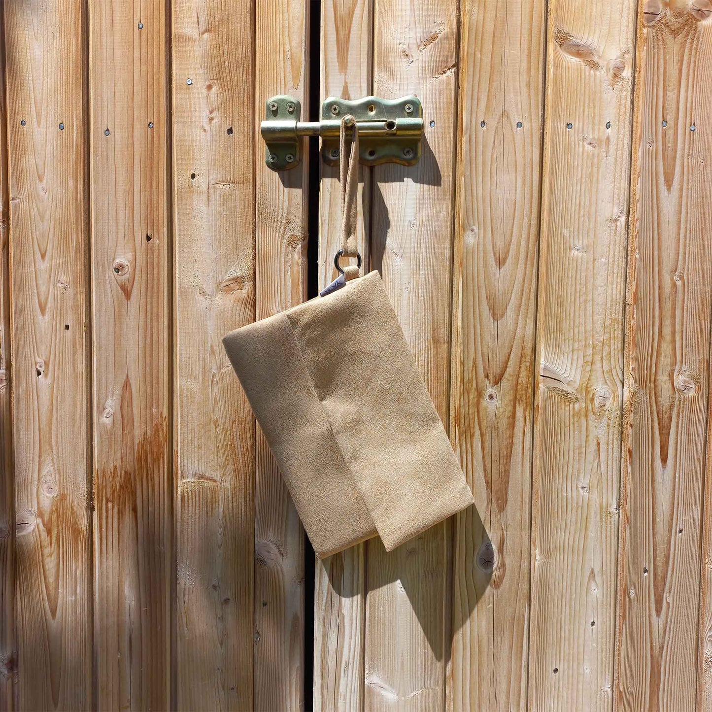 Handmade vegan suede clutch bag hanging from a shed lock.